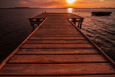 Wooden pier over sea against dramatic sky during sunset