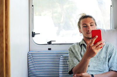 Portrait of man using mobile phone while sitting on window