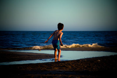 Rear view of boy on beach against clear sky