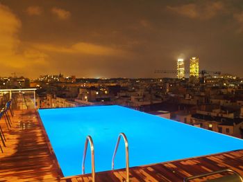 Swimming pool by cityscape against sky