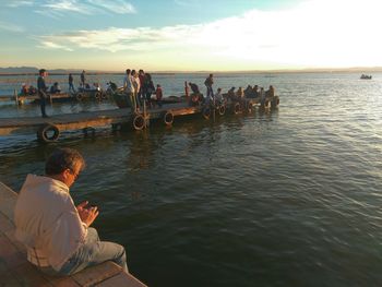 People sitting on pier over sea during sunset