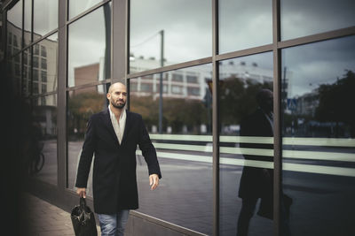 Mid adult businessman with briefcase walking against building in city