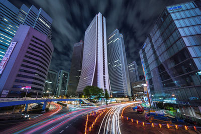 Light trails on city street amidst buildings against sky