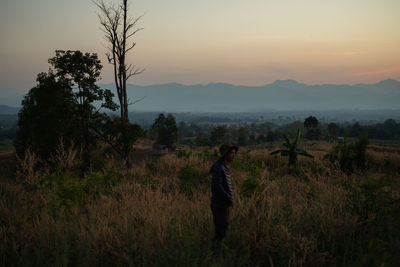 Man standing on field against sky during sunset