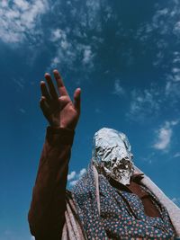 Low angle view of woman with covered face standing against sky