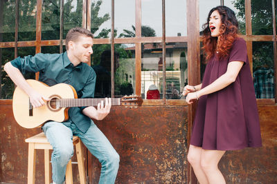 Man playing guitar while friend singing on sidewalk