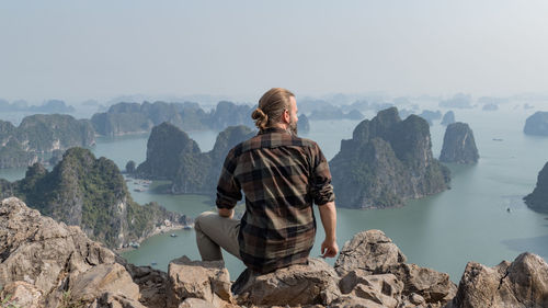 Man looking at view while sitting on mountain against sky