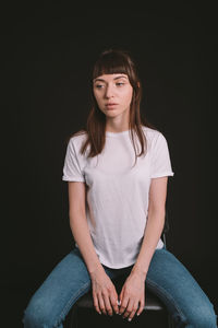 Portrait of young woman sitting against black background