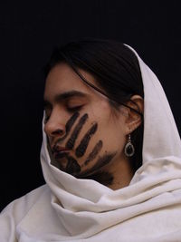 Close-up of young woman with handprint on face against black background