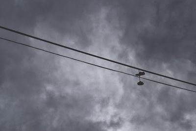 Low angle view of bird on cable against storm clouds