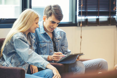 A couple sits in the hotel lobby, looking at a tablet computer.