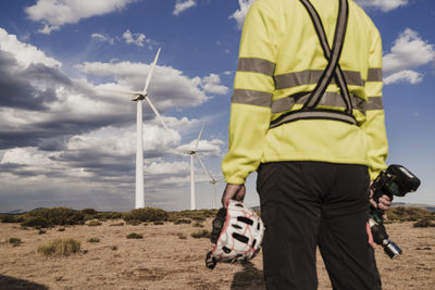 Technician holding work tool and helmet standing at wind farm