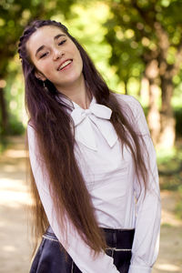 Portrait of smiling teenage girl with long brown hair standing in park