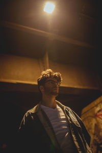 Low angle view of young man looking at illuminated lamp