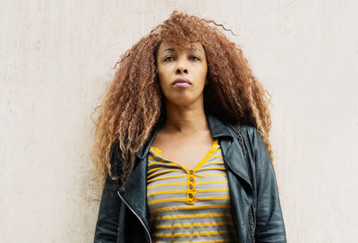 Portrait of woman with curly hair standing against wall