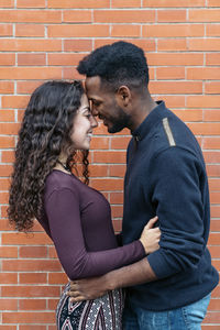 Side view of young couple standing against brick wall