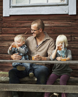 Father with two kids drinking juice in front of wooden house