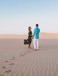 Rear view of woman walking at beach against clear sky