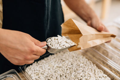 Top view of anonymous person pouring beans inside paper bag in local store