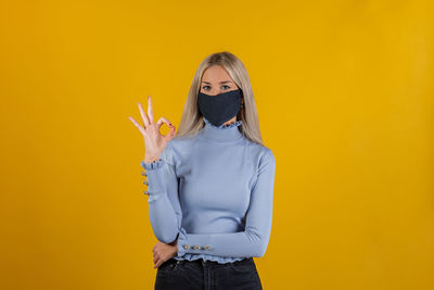 Woman standing against yellow wall with ok sign