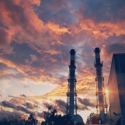 Low angle view of smoke stacks against sky during sunset