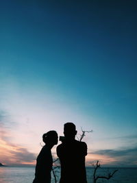 Silhouette couple standing at beach against blue sky