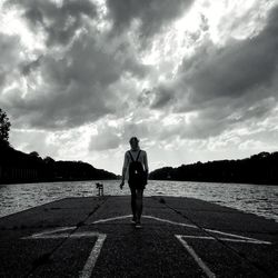 Rear view of woman walking on jetty in lake against cloudy sky