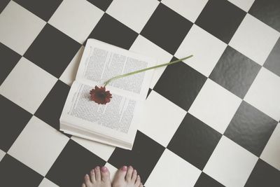 Low section of woman standing by red flower on book at checked floor