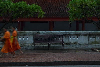 Rear view of people walking on bench against building