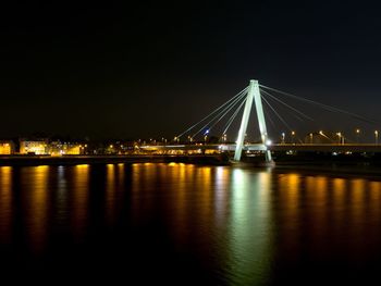 Illuminated bridge over river against sky at night