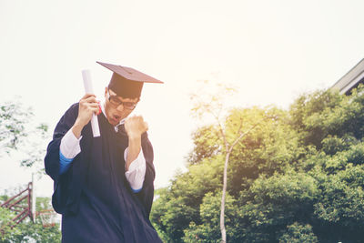 Cheerful student with clenched fist wearing graduation gown