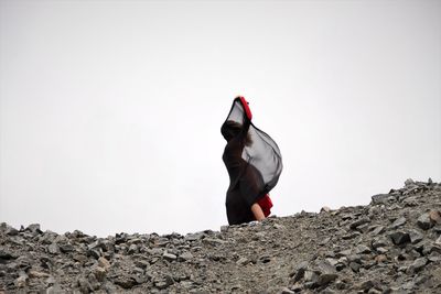 Low angle view of woman with black fabric standing against clear sky