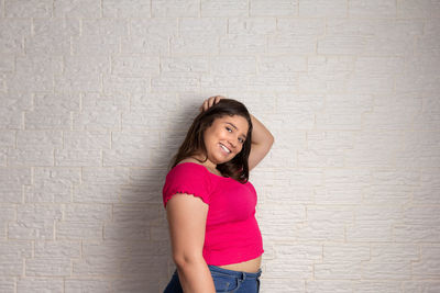 Portrait of smiling young woman standing against wall