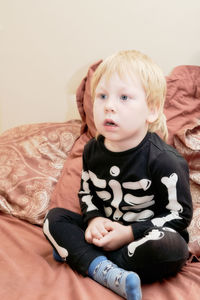 Cute boy sitting on bed at home