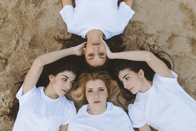 Young women touching female friend while lying down on sand