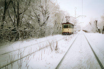 Tram on snowy railroad track by trees against sky