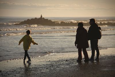 People standing on shore at beach against sky during sunset