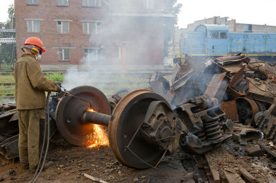 Rear view of worker using welding torch on old machine part