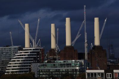 Low angle view of crane by buildings against sky