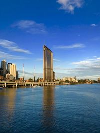 City buildings by river against blue sky