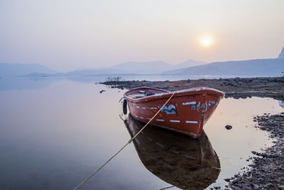 Fishing boat moored in sea against sky during sunset