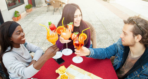 High angle view of friends toasting drinks while sitting at sidewalk cafe