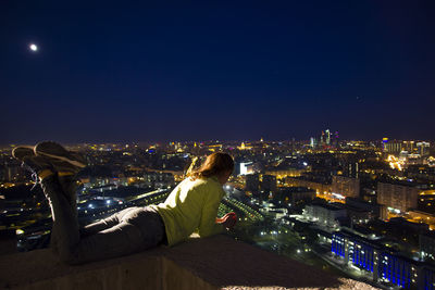 Woman lying on terrace in illuminated city at night