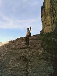 Low angle portrait of mature man with backpack showing peace sign while climbing mountain