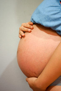 Midsection of pregnant woman in nightwear standing against wall