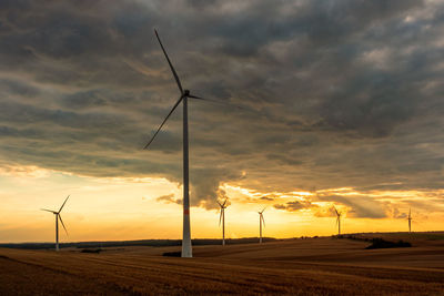 Wind turbines on field against sky during sunset