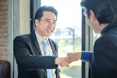 Businessmen doing fist bump by window at office