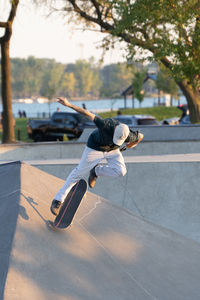 Male skate boarder practices tricks at an outdoor skatepark on a sunny day 