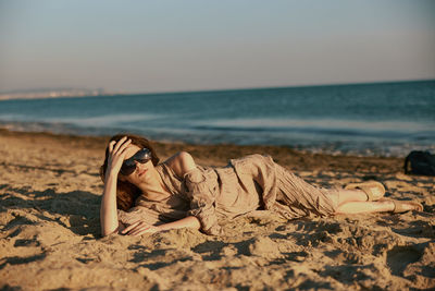 Low section of woman relaxing at beach against sky