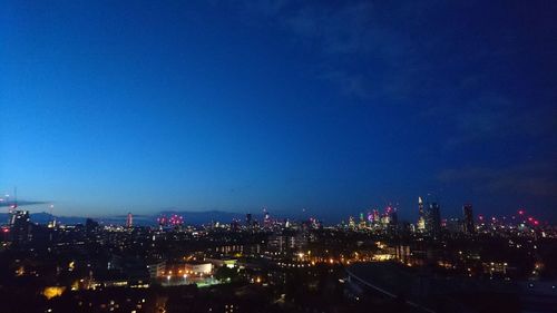 Illuminated cityscape against blue sky at night